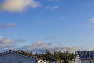 Obraz premium Beautiful view of roofs wooden villas on green forest trees and blue sky with light gray clouds backgrounds. Sweden. Europe.