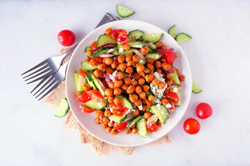 Healthy Mediterranean salad with chick peas. Above view with frame of ingredients over a white marble background.