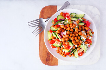 Healthy Mediterranean salad with chick peas. Overhead view on a serving platter over a white marble background.