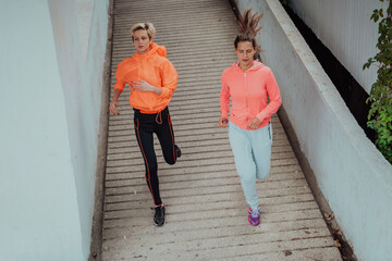 Obraz na płótnie Canvas Two women in sports clothes running in a modern urban environment. The concept of a sporty and healthy lifestyle