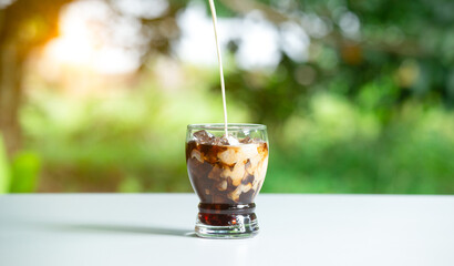 Ice coffee latte with cream being poured into it a glass. Milk coffee on white table.