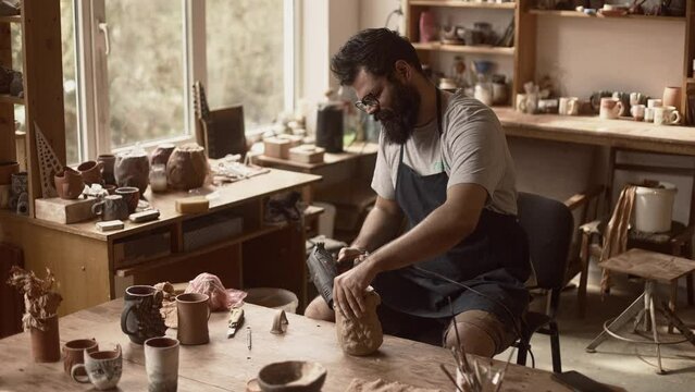 Man potter is working in pottery workshop, drying raw clay pot with an electric dryer before putting it to a kiln, ceramist lifestyle, beautiful pottery studio, Slow motion.