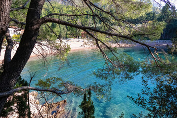 Scenic view on turquoise water of idyllic Queens beach framed by tree branches near Sveti Stefan, Budva Riviera, Adriatic Mediterranean Sea, Montenegro, Europe. Summer vacation in luxury seaside hotel