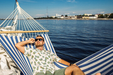 Handsome man rests in a hammock on a yacht. Leisure and fun in a water