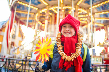 Obraz premium smiling boy with bagel beads, at the traditional Russian festival dedicated to the meeting of spring, the week of pancakes, Shrovetide. the child stands at the decorations for the Maslenitsa holiday