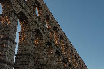 Obraz premium Roman aqueduct in stone with its arches illuminated by the evening light and isolated against the blue sky