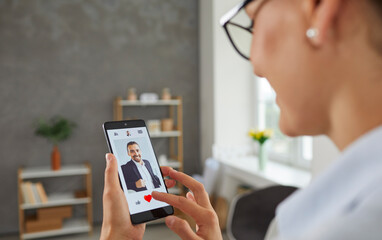 Woman holding a cellular telephone, visiting a modern online dating website or using a mobile phone app, looking at photos of different men and giving likes to the guys that she likes