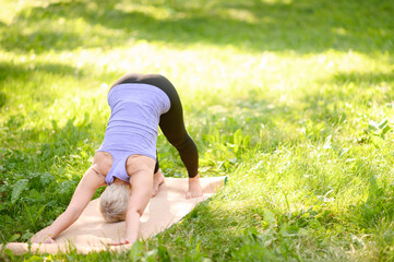 Middle age athletic attractive woman practicing yoga doing yoga in nature in d downward facing dog split pose.Adho mukha svanasana pose.The concept of stretching, healthy lifestyle, pilates.Copy space