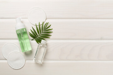 Foaming facial cleanser and micellar water with eco pads on wooden background, top view