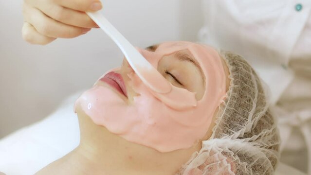 Beautician cosmetologist applying face alginate beauty pink mask. professional cosmetic procedure in a beauty clinic salon for client. Skincare and cosmetology spa concept.	