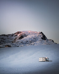 montagna innevata al tramonto con spazzaneve con casetta