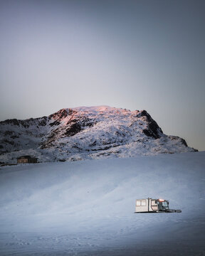 montagna innevata al tramonto con spazzaneve con casetta