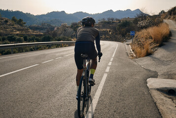 Silhouette of a sporty cyclist in a helmet and cycling kit.Cyclist is training on a gravel bike on...