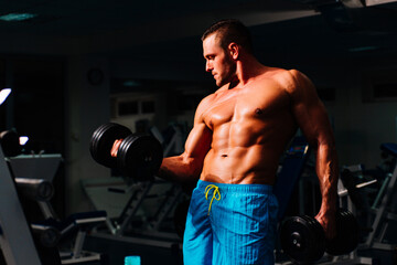 Fototapeta na wymiar Fit strong man doing biceps in gym. Portrait of young athlete doing exercise with dumbbell at the gym. Crossfit, sport and healthy lifestyle concept.