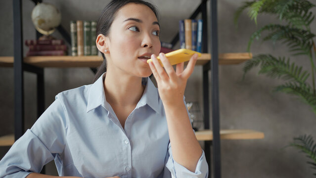 Close up portrait of smiling asian business woman recording a voice message to someone using smartphone