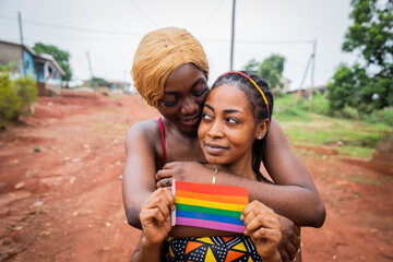 African lesbian women couple hugging, girlfriend holds a rainbow flag, homosexual love