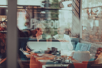 Photo through the glass of a group of business people sitting in a cafe and discussing business plans and ideas for new online commercial services