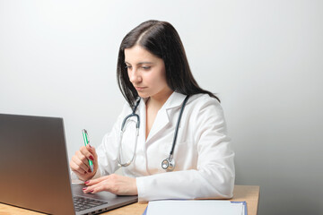 Female doctor, medic physician in white coat with stethoscope working on laptop at table