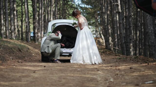 Just married couple newlyweds, bride and groom fixing engine of old timer car in the middle of the forest path, slow motion.