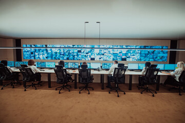 Group of Security data center operators working in a CCTV monitoring room looking on multiple monitors.Officers Monitoring Multiple Screens for Suspicious Activities