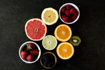 Dark background with an array of citrus such as grapefruit, oranges, lemon, lime, and several berries such as raspberries, blackberries, and strawberries