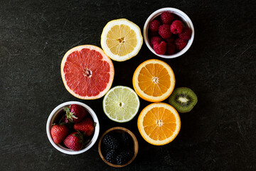 Dark background with an array of citrus such as grapefruit, oranges, lemon, lime, and several berries such as raspberries, blackberries, and strawberries