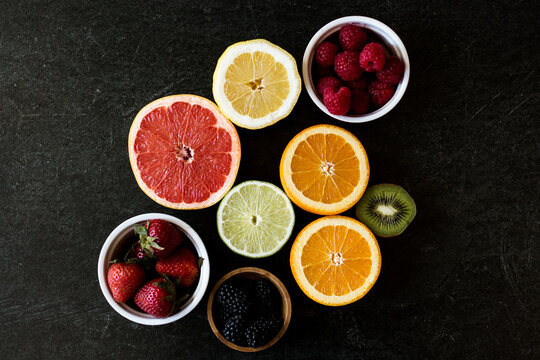 Dark background with an array of citrus such as grapefruit, oranges, lemon, lime, and several berries such as raspberries, blackberries, and strawberries