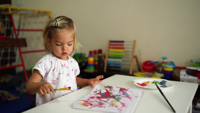 Little girl draws with a brush on paper at the table
