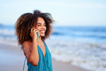 young brazilian black woman with afro hairstyle talking on the cell phone on the beach with ocean...