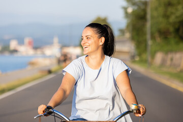 Happy smiling woman riding bicycle along the coast at summer