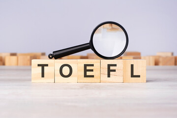 woden blocks with a magnifying glass text: TOEFL. Test Of English As A Foreign Language