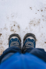 A child, a boy in boots, shoes stands on the ground with snow in winter. Photography, lifestyle.