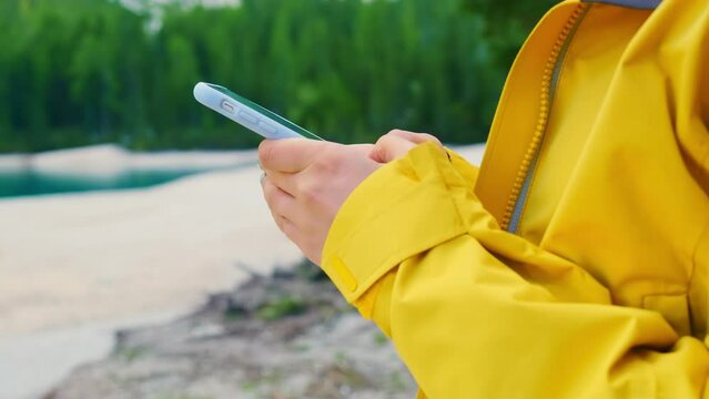 Woman uses a smartphone standing near the lake. Tourist shares photos via social networks. 