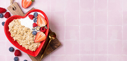 Oatmeal porridge with berry and yogurt in red bowl in the heart shape, top view. Oat flakes healthy breakfast meal. Clean eating, dieting, healthy food. Copy space © missmimimina
