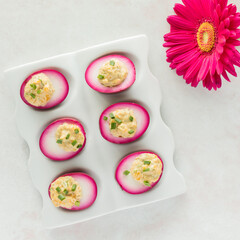 Top down view of a platter of bright pink devilled eggs. An Easter concept.
