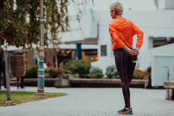 Fit attractive woman in sportswear stretching one leg before jogging on the footpath outdoor in summer among greenery. Workout, sport, activity, fitness, vacation and training concept.