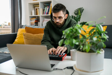 Man recording electronic music track with portable midi keyboard on laptop computer in home studio. Producing and mixing music beat making and arranging audio content with professional audio devices