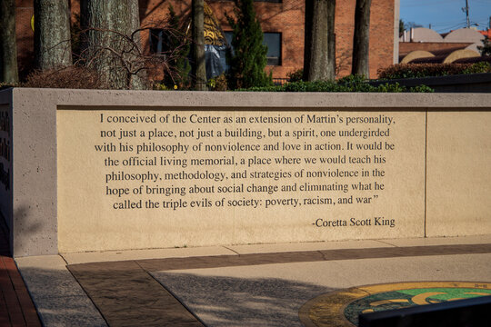 A gorgeous winter landscape at The King Center with a red brick sidewalk, bare trees, lush green plants, a staircase and the words of Coretta Scott King on the wall with blue sky in Atlanta Georgia