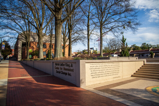 A gorgeous winter landscape at The King Center with a red brick sidewalk, bare trees, lush green plants, a staircase and the words of Coretta Scott King on the wall with blue sky in Atlanta Georgia