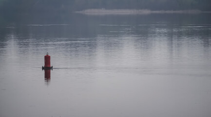 A minimalistic buoy on the Dnieper river peeks out of the water, on a cloudy spring day