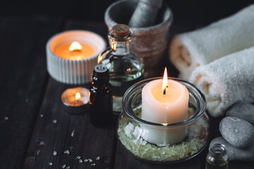 Obraz na płótnie Canvas Spa setting with essential oil, candle, sea salt, pebbles, towel on dark wooden background. Massage, aromatherapy. Natural organic ingredients for relaxation, detention. Wellness in salon concept