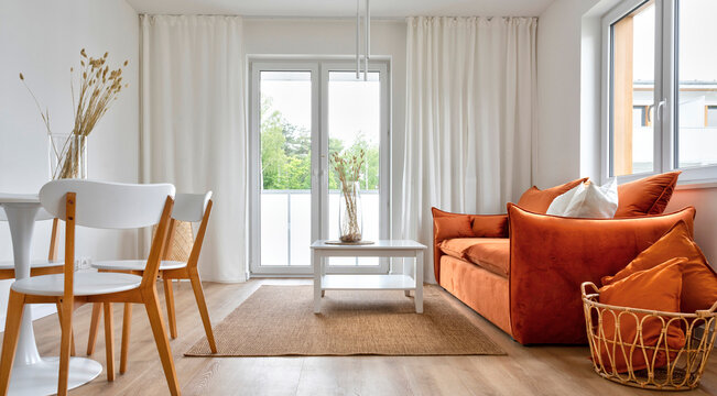 Minimalism In Modern Interior Of Living Room With Window And White Curtains. Modern Red Sofa With Pillows And Table With Chairs On Wooden Floor.