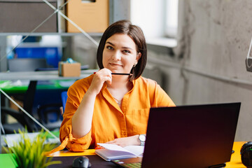 a brunette woman in an orange blouse works on a laptop at desk in the office