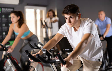 Fototapeta na wymiar Focused sporty young guy working out on stationary bicycle in gym. Physical activity and fitness concept