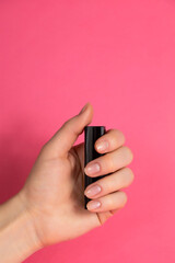 Female hand holding lipstick. Close up. Pink background.