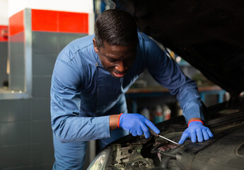 African car mechanic with screwdriver repairing car engine under the hood in auto service