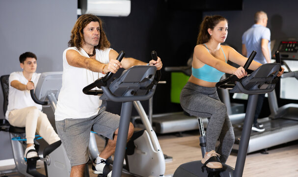 Group of people of different ages working out on stationary bicycle in gym. Physical activity and fitness concept