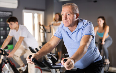 Focused aged man leading healthy active lifestyle doing cardio workout on exercise bike in gym
