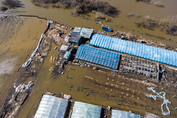 Agricultural farm with greenhouses in a field flooded during a strong spring flood as a result of a river flood, aerial view