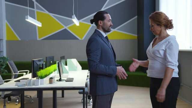 In the office, a man and a woman, colleagues, a boss and an employee shake hands, smile, nod their heads.